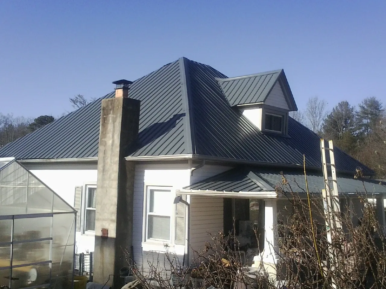 Dark blue standing seam metal roof on a white farmhouse with dormer — Slate & Tile Roof Repair by Roofing Brothers in Riesel