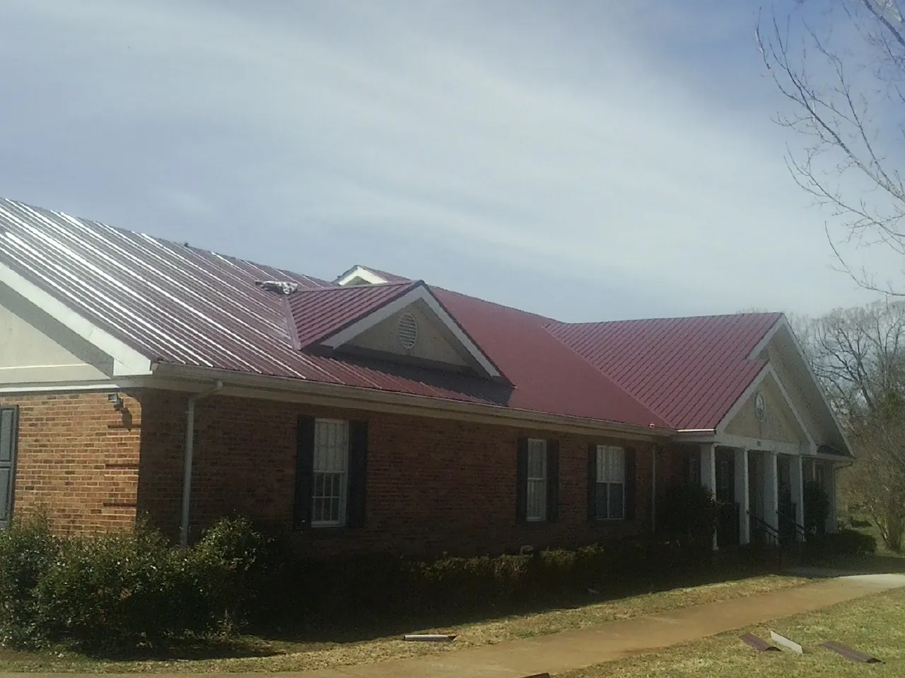 Red metal roof with gabled entries on a long brick building, from a Hail Damage Roof Repair job in Riesel