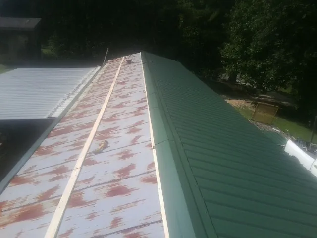 Old rusted panels beside newly installed green metal roofing — Wind Damage Roof Repair by Roofing Brothers in Riesel