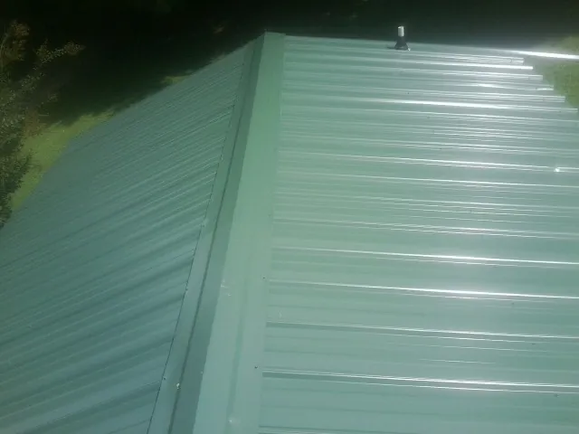 New green metal panels meeting at the ridge of a roof — Flat Roof Repair work by our crew in Riesel