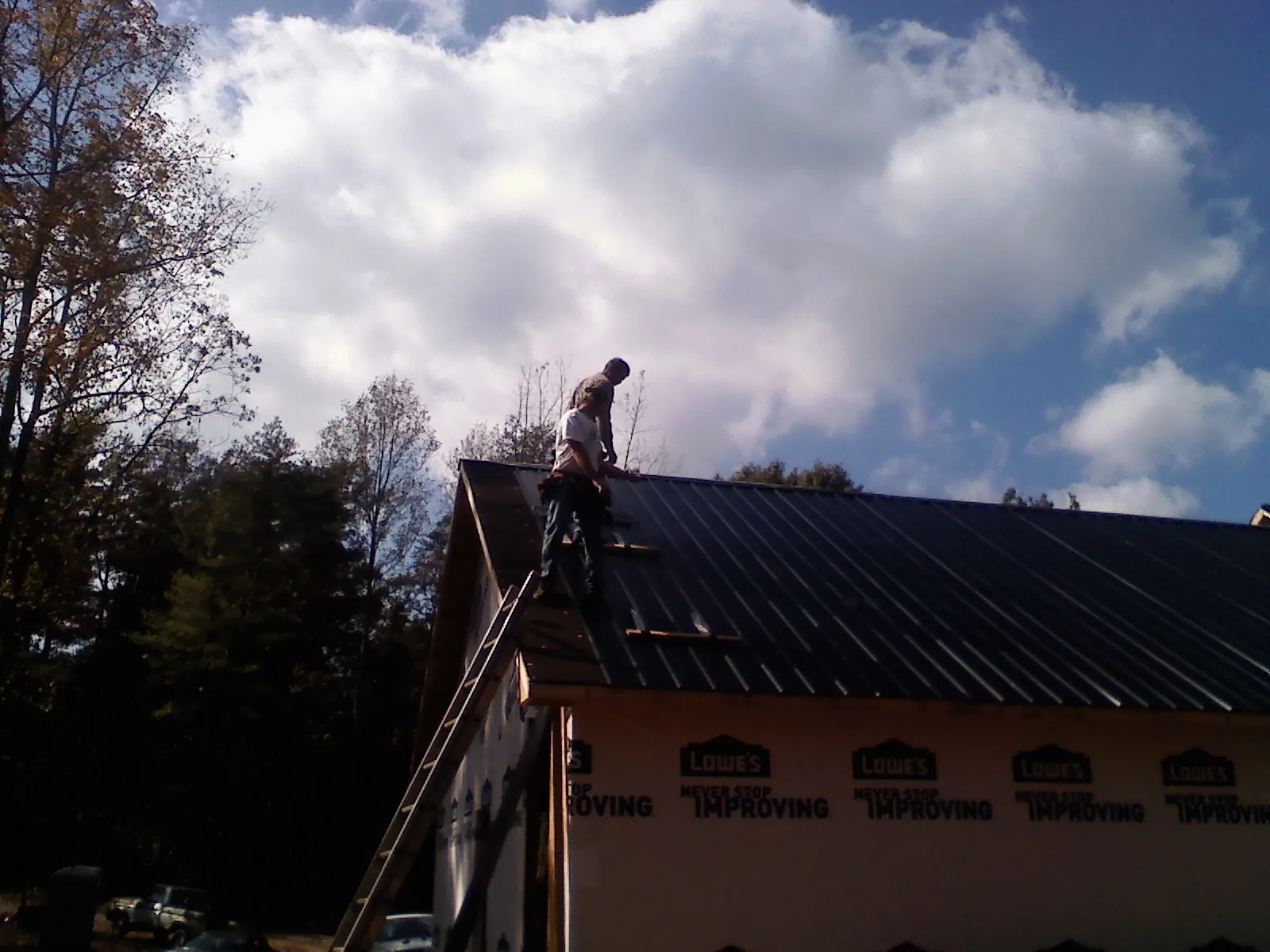 Roofer fastening dark metal panels high against a cloudy sky, from a Roof Inspection job in Riesel