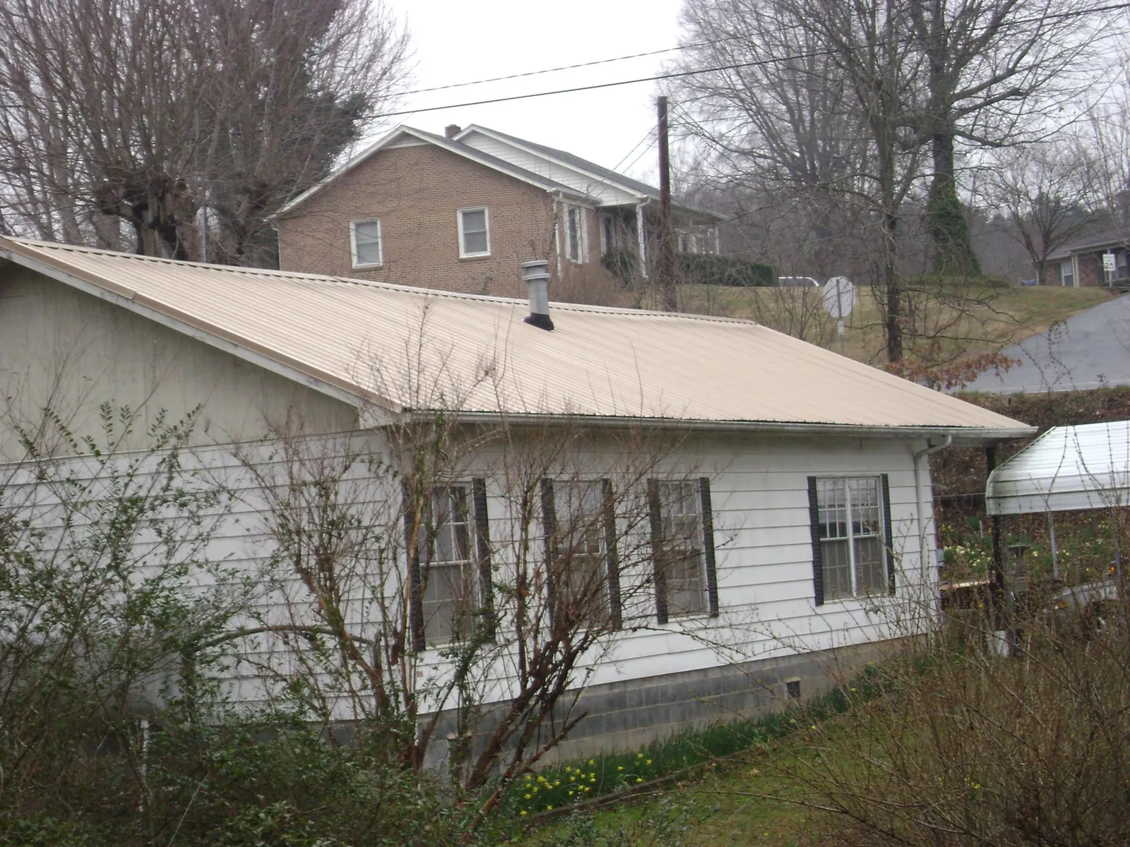 Tan metal roof on a white sided house set into a hillside — Commercial Roofing by Roofing Brothers in Riesel